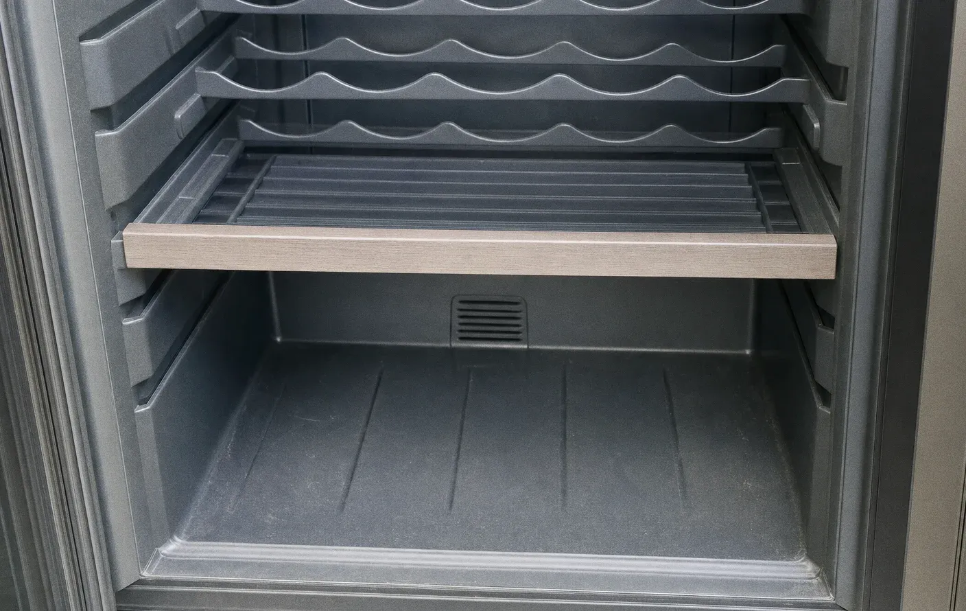 Inside an empty wine cabinet, moulded scalloped bottle racks above a wood-fronted pull-out shelf